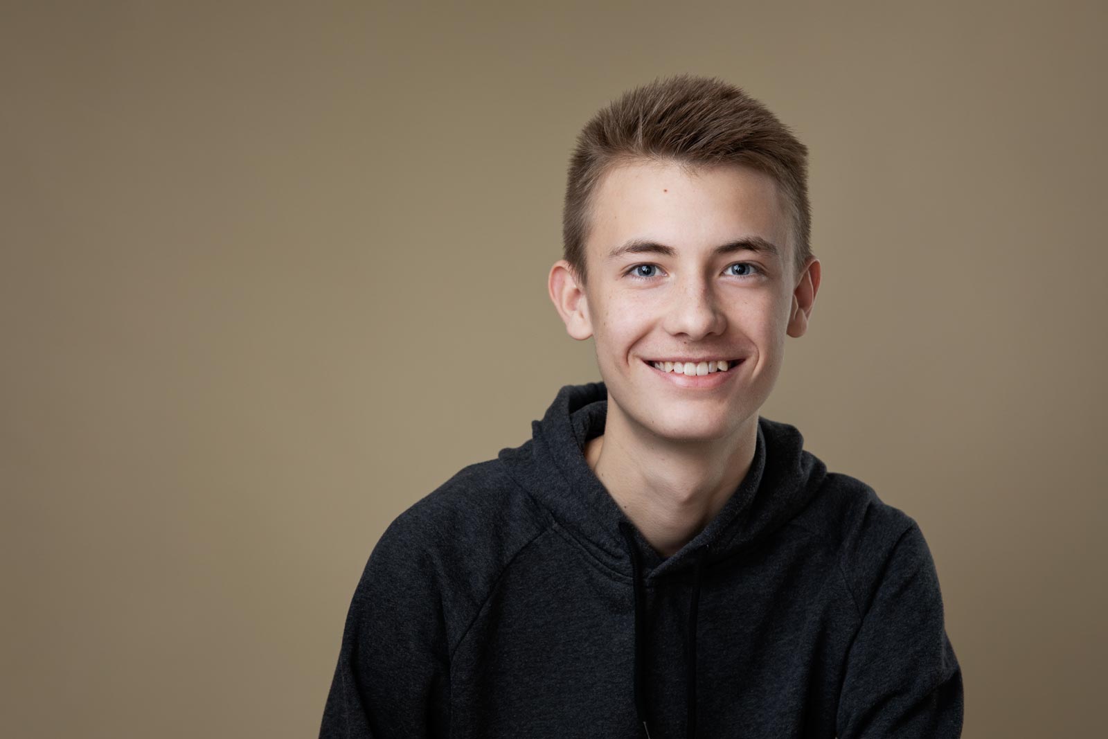 teenager sidder casual og smiler foran en brunlig baggrund
