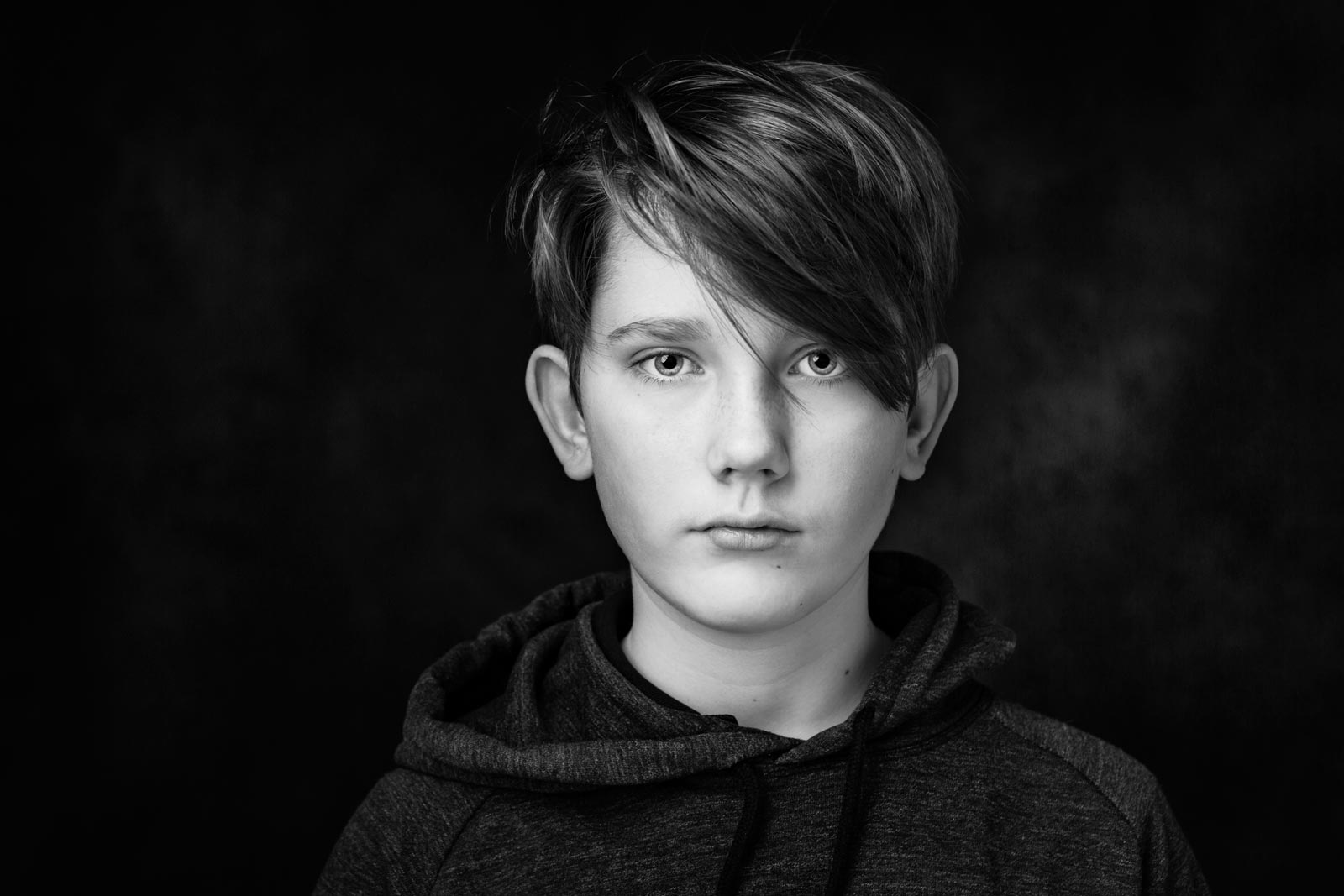 Sort hvidt billede af teenager dreng uden smil på mørk baggrund